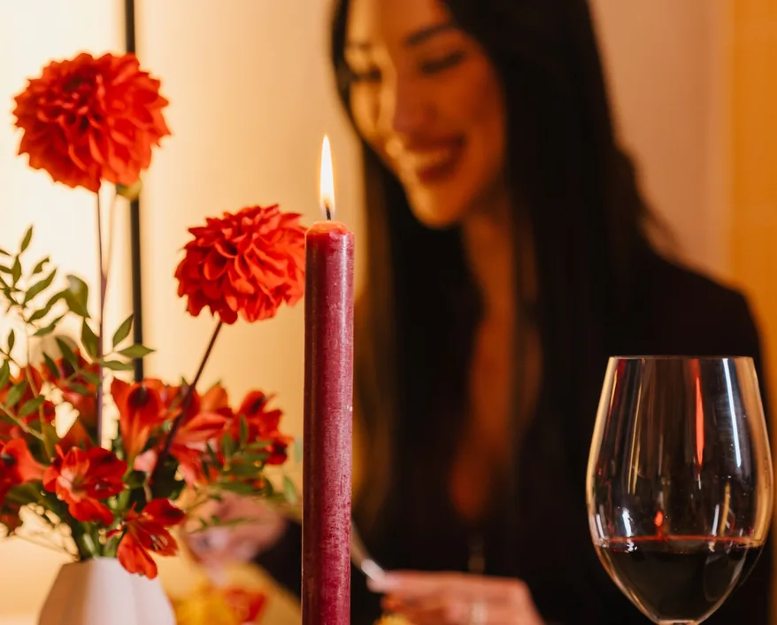 A candle in a burgundy bow candlestick and red dahlias on a Christmas table at Mimosa
